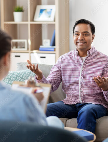 psychology, mental therapy and people concept - happy smiling young indian man patient and woman psychologist at psychotherapy session